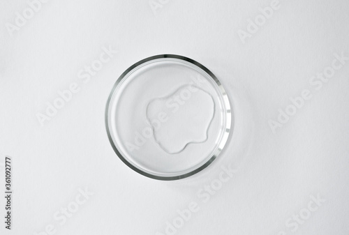 Pure liquid spot in glass petri dish on white background with copy space, top view. Concept science laboratory