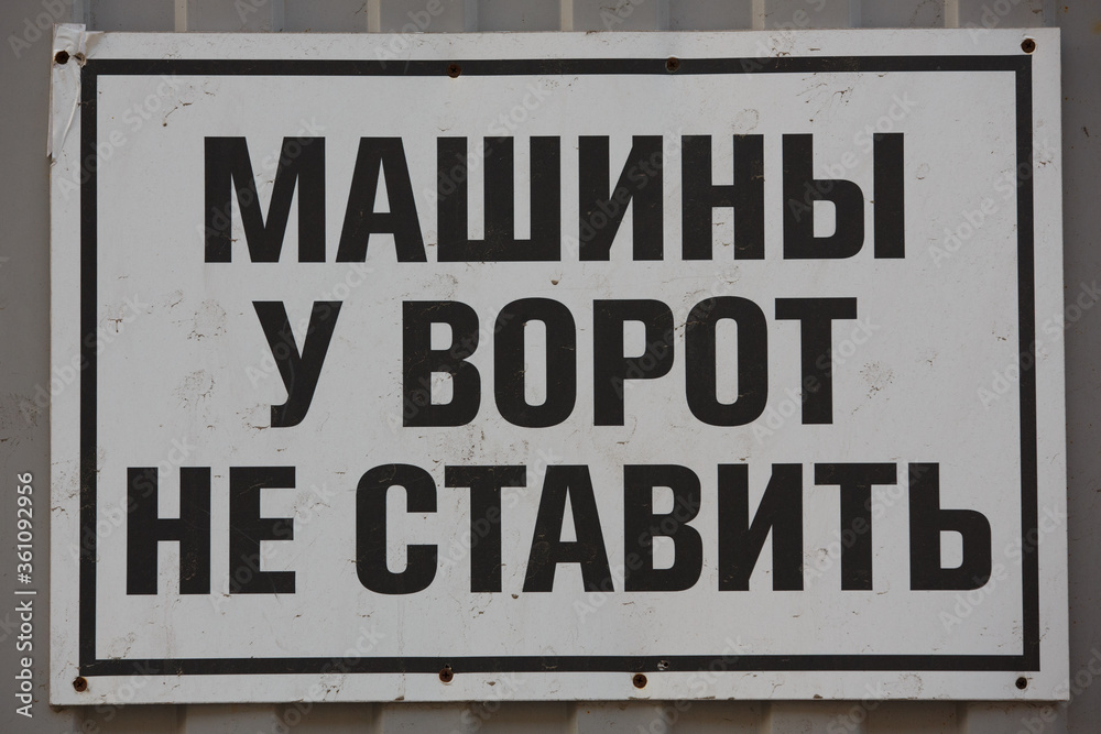 a close up shot of a black warning sign on a white background saying in Cyrillic russian DO NOT PARK CARS IN FRONT OF THE GATES