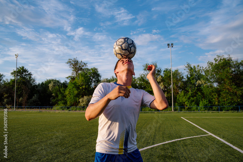 Young male soccer player juggles a ball with his head on a soccer field