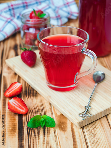Strawberry compote in a transparent glass mug on a wooden table against the background of berries and a bottle