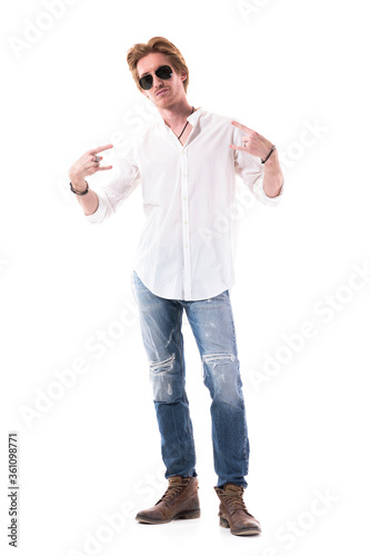 Young serious handsome stylish man showing heavy metal horns sign. Full length portrait isolated on white background. 