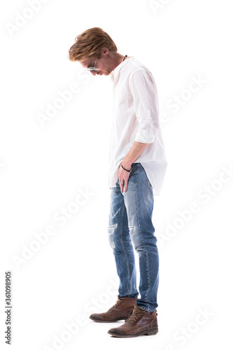 Side view of sad disappointed young red hair stylish man looking down thoughtful. Full length portrait isolated on white background. 