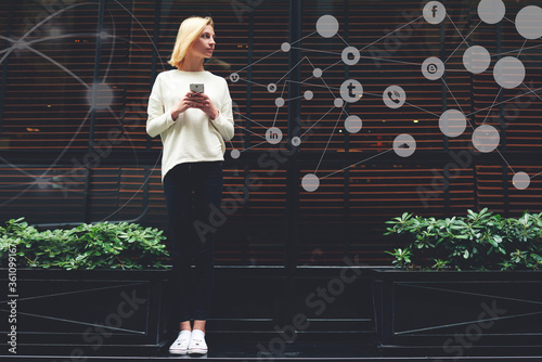 Full length portrait of gorgeous young woman holding smartphone in hand and looking to copy space with popular applications icons with infographics elements design. Personalized multimedia program