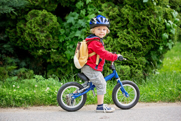 Cute toddler boy with blue helmet, riding balance bike on the street