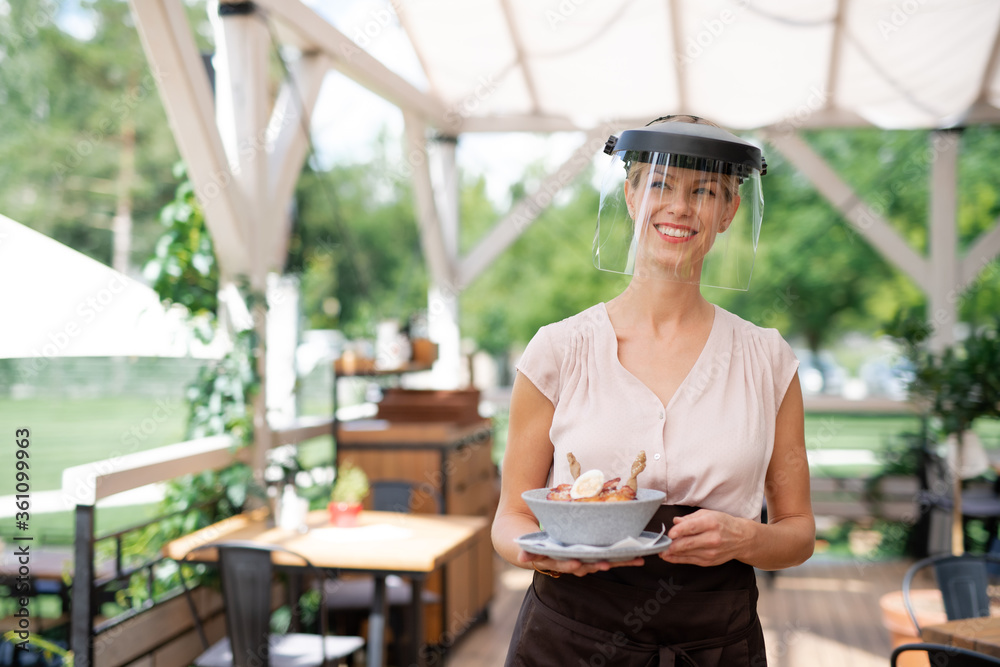 Waitress with protective face shield serving customers outdoors on terrace restaurant. Waitress with protective face shield serving customers outdoors on terrace restaurant.
