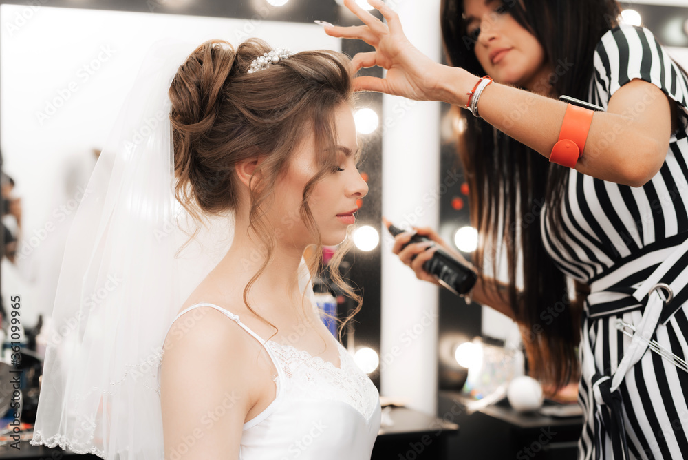 hairdresser makes styling a beautiful girl bride using a spray