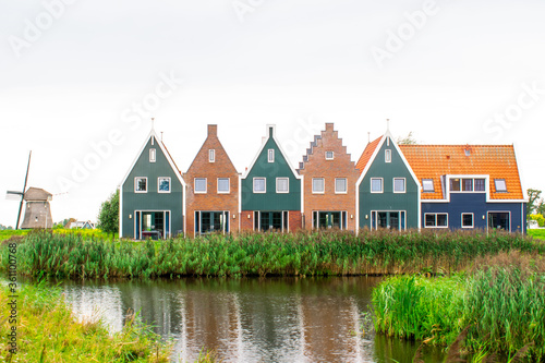 Colorful Traditional Dutch houses on the waterfront with old style windmill at the back, in a small beautiful town of Volendam in North Holland, Netherlands
