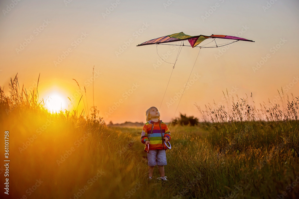 Blond child, toddler boy, running in field on sunset, holding flowers Blond child, toddler boy, running in field on sunset, holding flowers