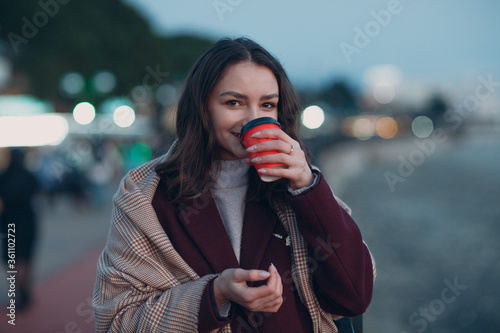 Young beautiful woman in coat and scarf with coffee cup outdoor.