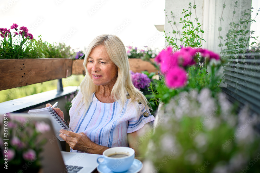 Active senior woman with laptop working on balcony, home office.