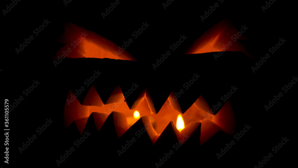 Halloween pumpkin with candles glowing inside at black background
