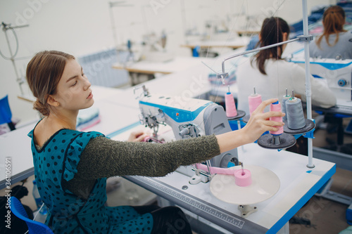 Young beautiful seamstress sews on sewing machine in factory