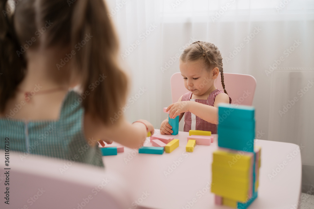 Lovely kids plaing with colorful wodden blocks in a creative educational game as they stand at a pink table Lovely kids plaing with colorful wodden blocks in a creative educational game as they stand at a pink table