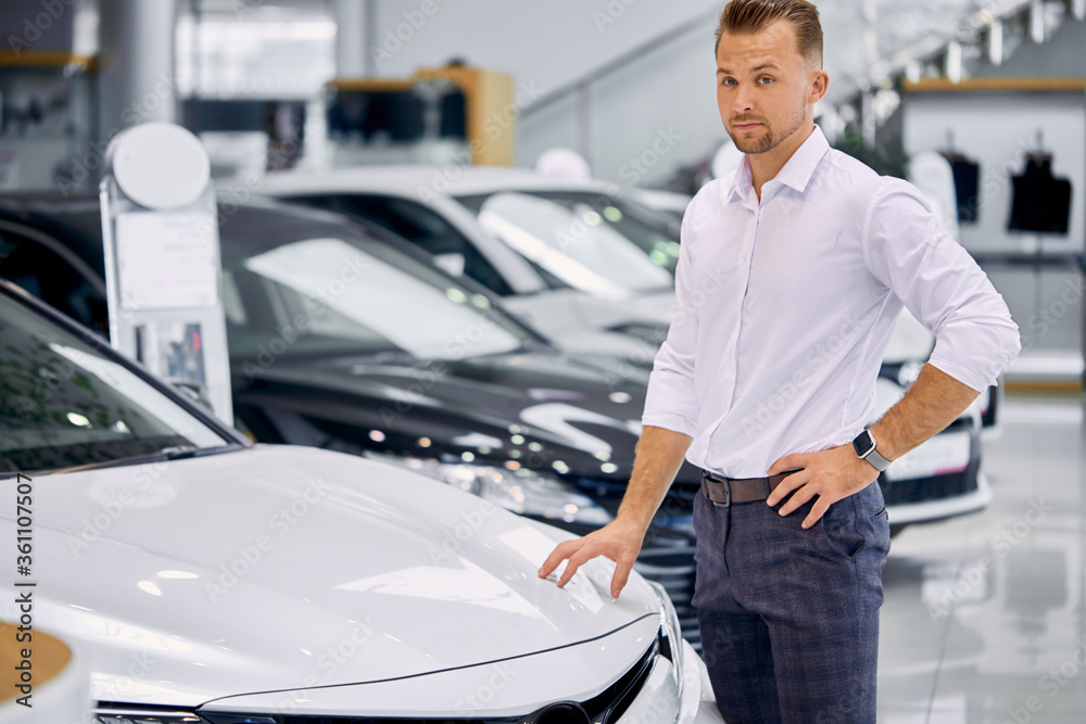 portrait of happy caucasian client man buying new car in car store. luxurious white car is on exhibition in dealership portrait of happy caucasian client man buying new car in car store. luxurious white car is on exhibition in dealership