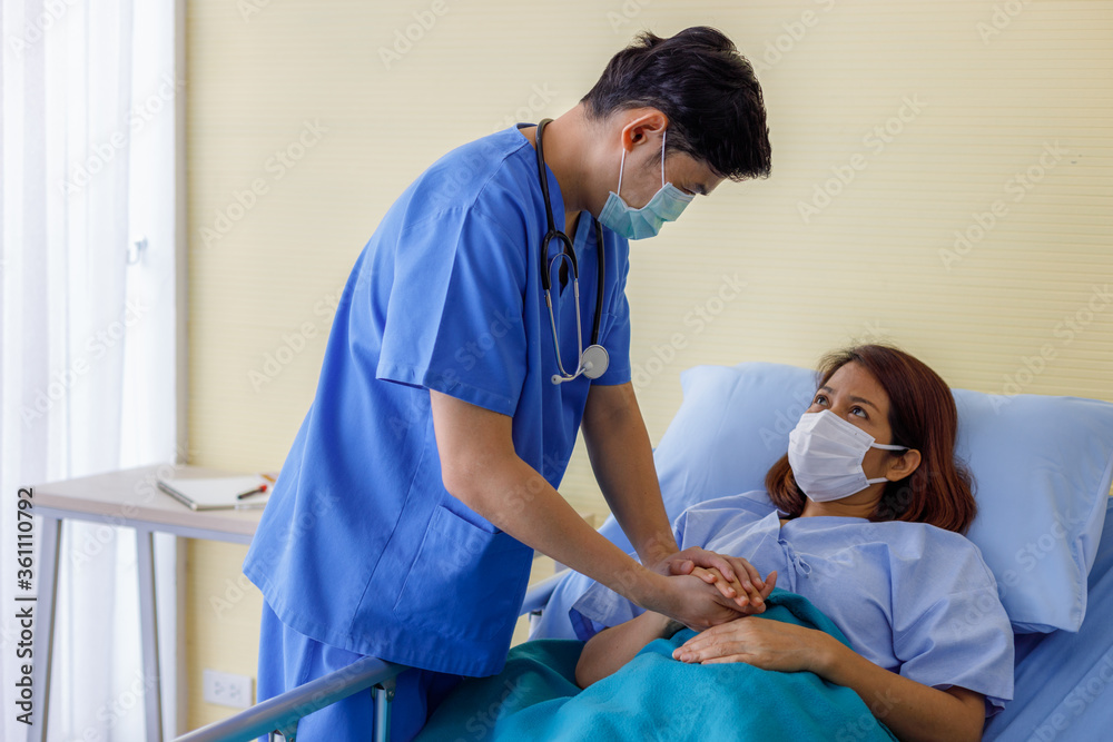 Fototapeta premium Asian male doctors wear uniforms and medical masks, holding hands with middle-aged female patients to encourage patients.