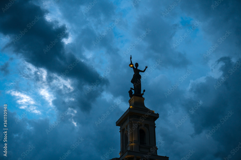 Statue of a woman with a lantern on the background of a stormy sky