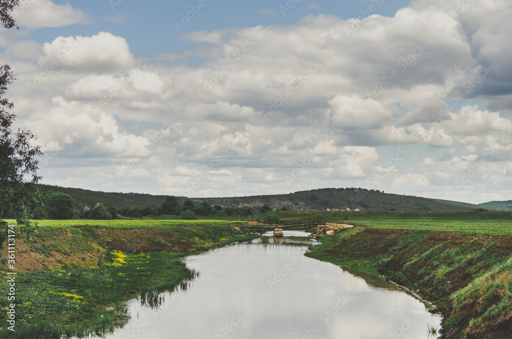 River side landscape with bridge over the river and fluffy clouds on a bright blue sky in a rural Moldovan setting