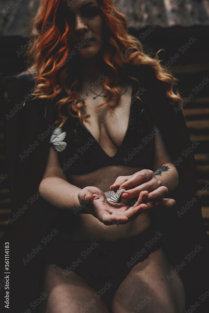 A red-haired girl stands in a forest in a raincoat with a hood with a naked chest A red-haired girl stands in a forest in a raincoat with a hood with a naked chest