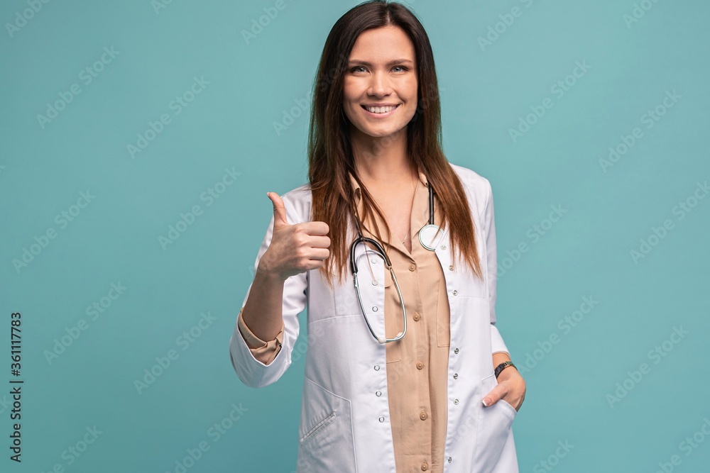 Friendly female doctor with thumbs up - isolated over light blue. Friendly female doctor with thumbs up - isolated over light blue.