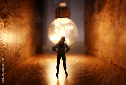 Surreal image of person in dark corridor looking at glowing light bulb. Concept of finding the right idea  or way out