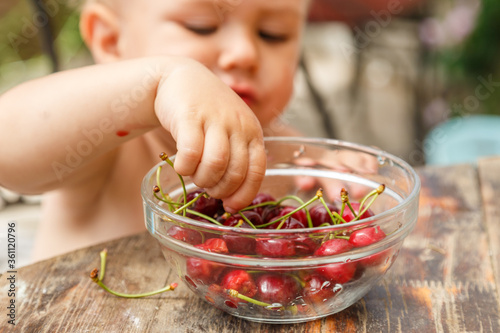 Cute happy boy taking sweet cherry from the plate, outdoor in garden