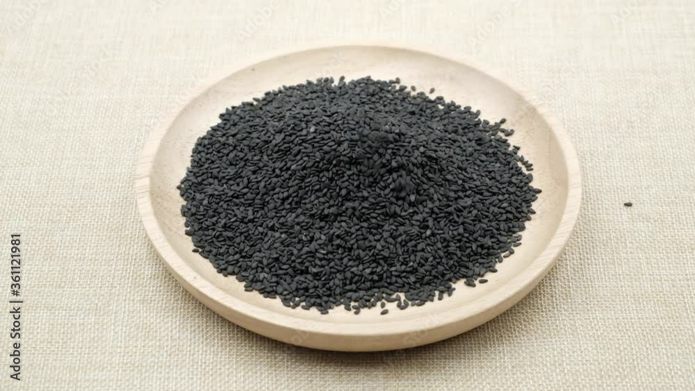 Sprinkling black sesame seeds on a wooden plate. black organic sesame seeds. Sprinkling black sesame seeds on a wooden plate. black organic sesame seeds.