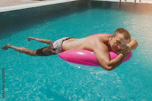 Happy man is sleeping and relaxing on big pink inflatable ring at swimming pool on summer day.