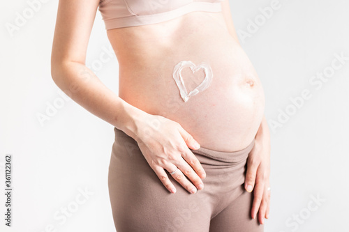Close up shot of pregnant woman, heart shape stretch mark cream, mother expecting twins over grey background