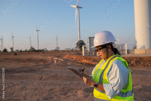 women engineer working and holding the report at wind turbine farm Power Generator Station on mountain,Thailand people