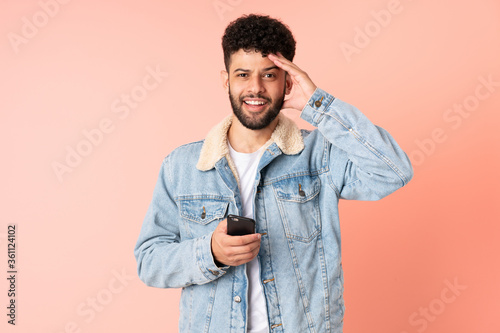 Young Moroccan man using mobile phone isolated on pink background with surprise expression © luismolinero
