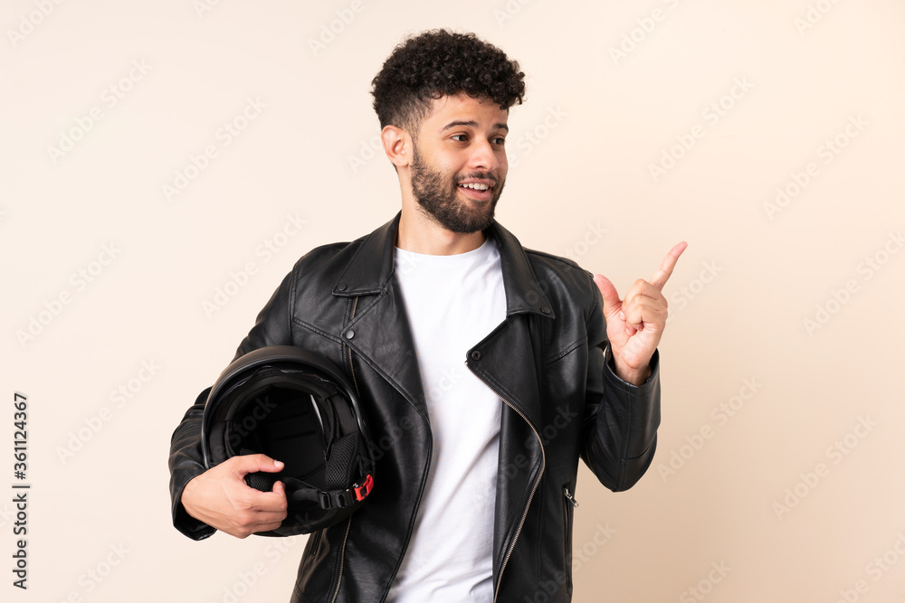 Young Moroccan man with a motorcycle helmet isolated on beige background intending to realizes the solution while lifting a finger up Young Moroccan man with a motorcycle helmet isolated on beige background intending to realizes the solution while lifting a finger up