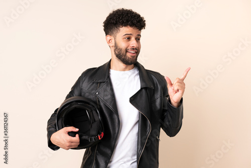 Young Moroccan man with a motorcycle helmet isolated on beige background intending to realizes the solution while lifting a finger up