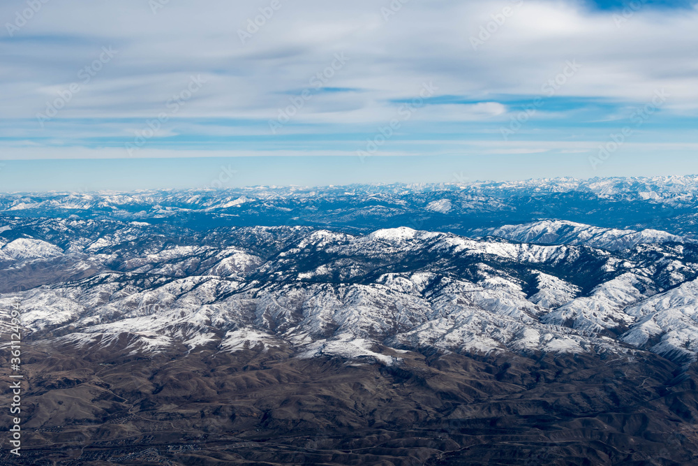Obraz premium Aerial View of Idaho mountains from the sky while inside an airplane. View of brown mountains and trees covered with snow