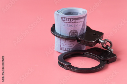 twisted wad of dollars buttoned with handcuffs on a pink background