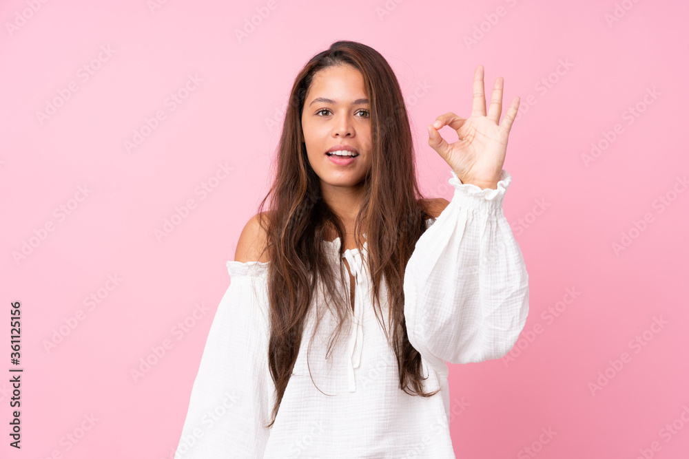 Young Brazilian girl over isolated pink background surprised and showing ok sign Young Brazilian girl over isolated pink background surprised and showing ok sign