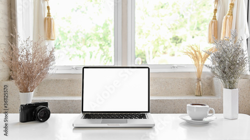 Laptop with blank screen on white table with coffee cup. Home interior or office background. © Kittipong