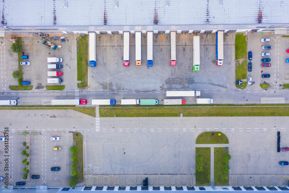 Aerial view of goods warehouse. Logistics center in industrial city zone from above. Aerial view of trucks loading at logistic center. View from drone.