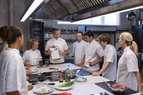 Senior male chef showing paper to all other chefs at restaurant kitchen photo