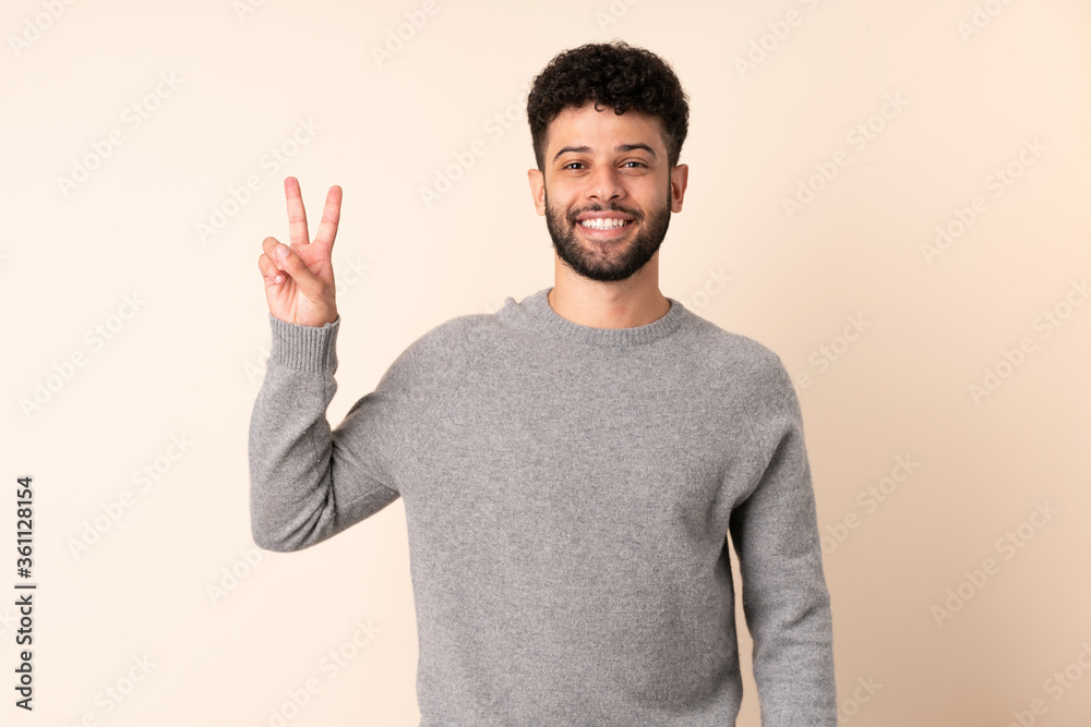 Young Moroccan man isolated on beige background smiling and showing victory sign Young Moroccan man isolated on beige background smiling and showing victory sign