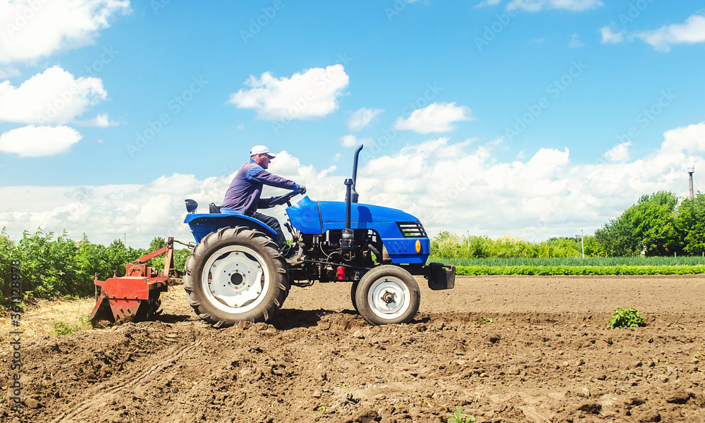 Farmer drives a tractor with a milling machine. Loosens, grind and mix soil on plantation field. Loosening surface, cultivating the land. Farming, agriculture. Field preparation for new crop planting. Farmer drives a tractor with a milling machine. Loosens, grind and mix soil on plantation field. Loosening surface, cultivating the land. Farming, agriculture. Field preparation for new crop planting.