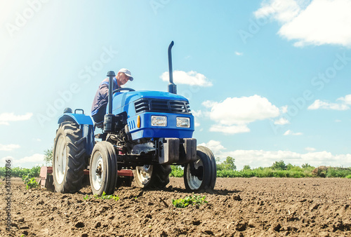 The farmer works on a tractor. Loosening the surface, cultivating the land for further planting. Grinding and loosening soil, removing plants roots from last harvest. Cultivation technology equipment. photo