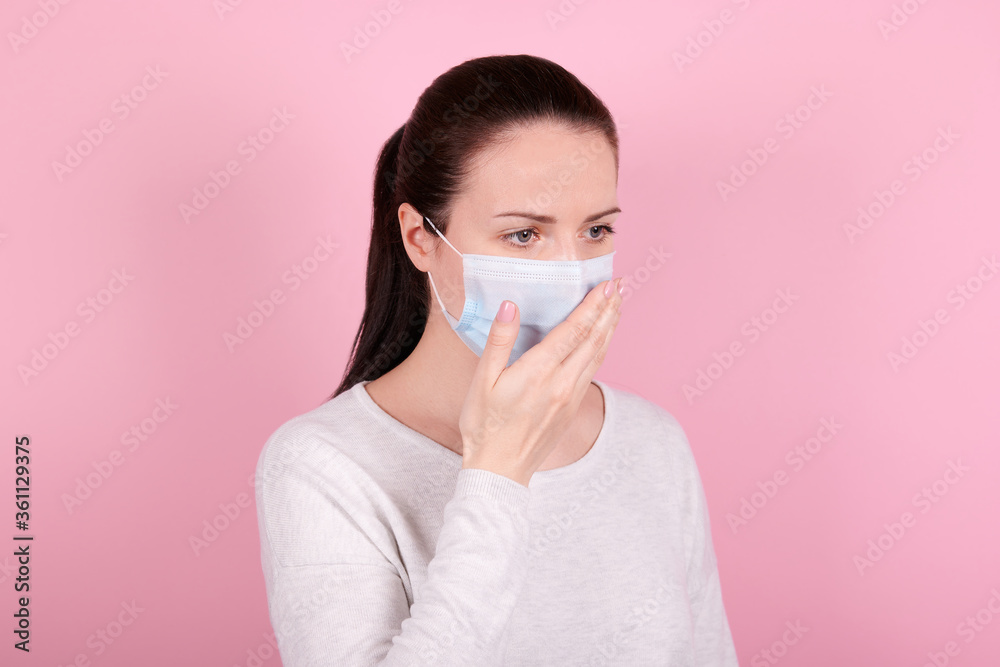 Portrait of a brunette girl in a medical mask coughs. Isolated on pink background. Portrait of a brunette girl in a medical mask coughs. Isolated on pink background.