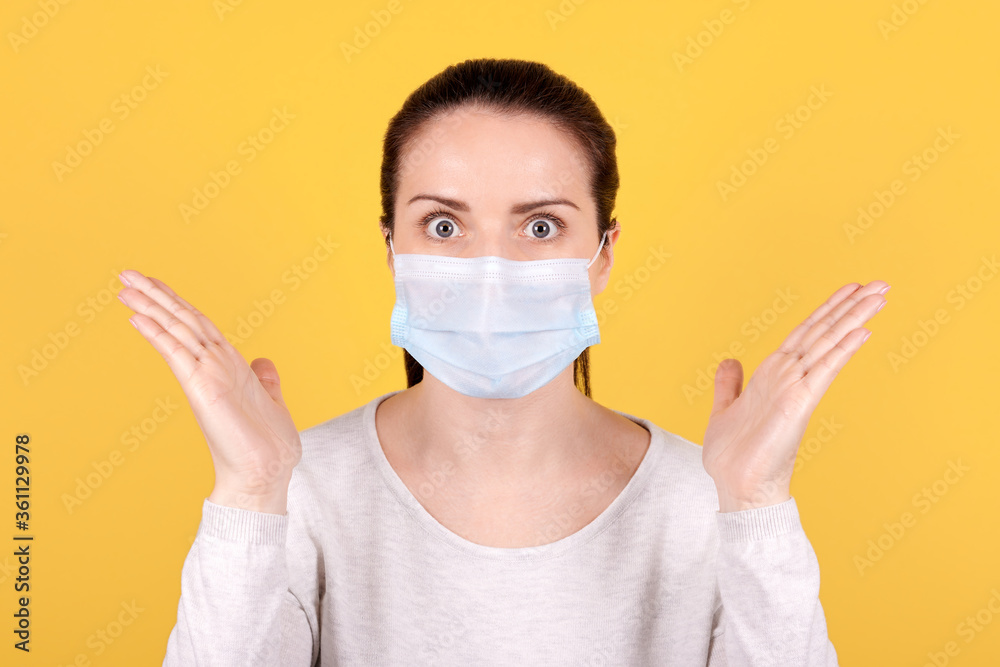 Portrait of a brunette girl in a medical mask spreads her arms to the sides in surprise. Portrait of a brunette girl in a medical mask spreads her arms to the sides in surprise.
