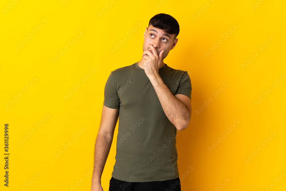 Young Colombian man isolated on yellow background having doubts and with confuse face expression Young Colombian man isolated on yellow background having doubts and with confuse face expression