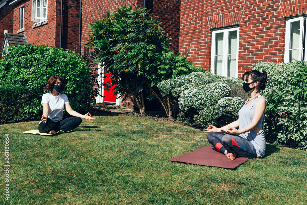 Two woman are doing yoga while wearing face masks and keeping the social distance at the garden, stay home and keep the distance concept, new normal
