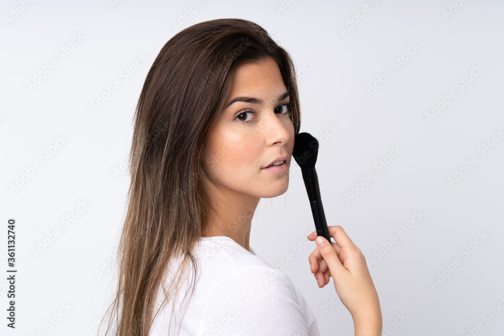 Teenager girl over isolated background holding makeup brush Teenager girl over isolated background holding makeup brush