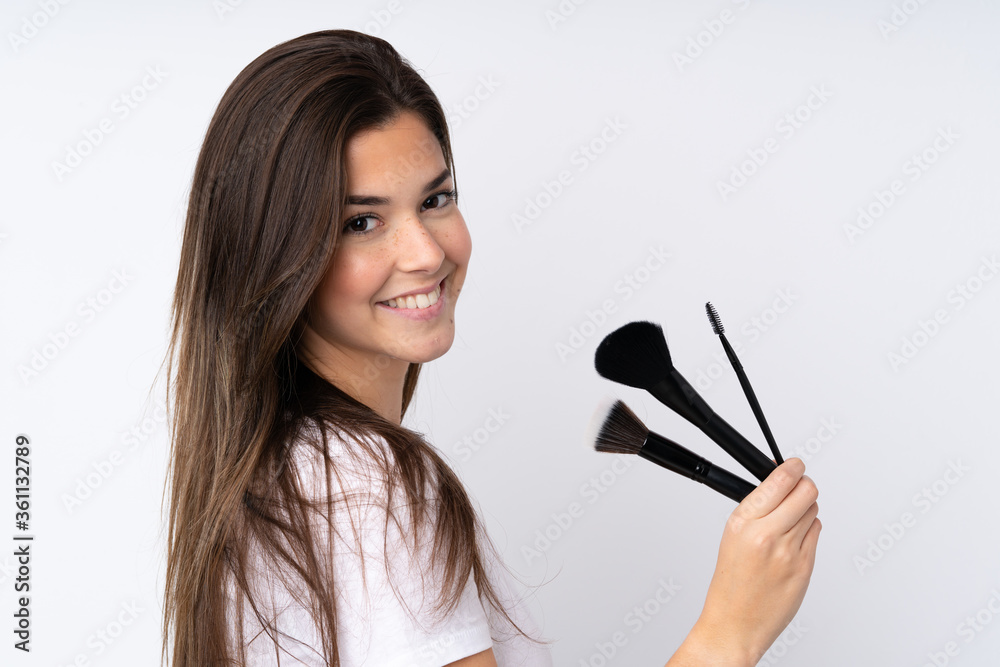 Teenager girl over isolated background holding makeup brush Teenager girl over isolated background holding makeup brush
