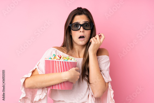 Teenager girl over isolated pink background with 3d glasses and holding a big bucket of popcorns © luismolinero