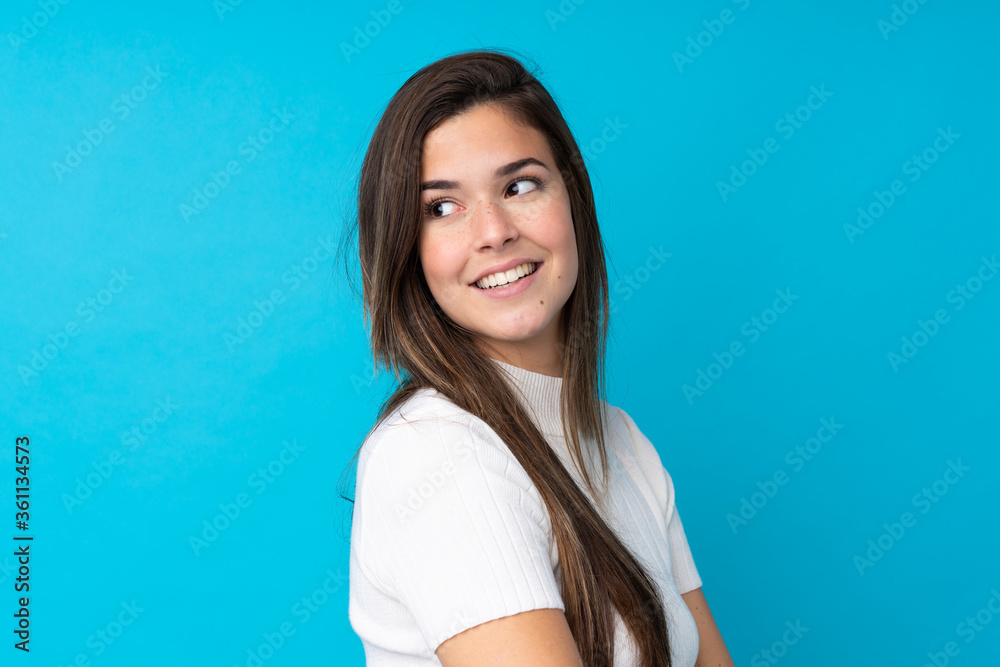 Fototapeta premium Teenager girl over isolated blue background with arms crossed and happy