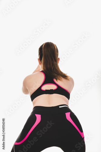Caucasian young woman with brown hair, doing squats during a sport session at home, wearing sportswear